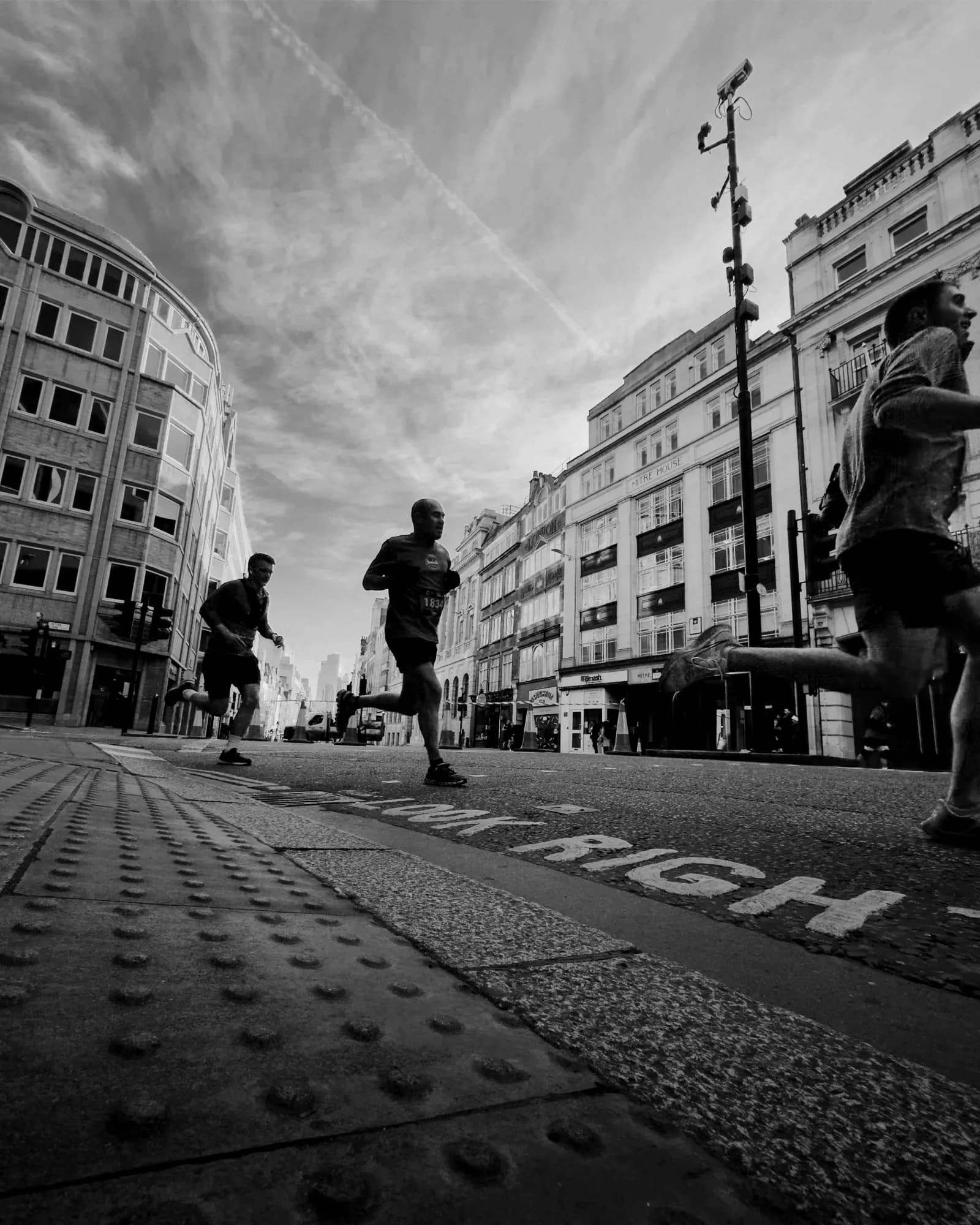 London Marathon runners crossing a central London street, photographed from kerb level beside the course.
