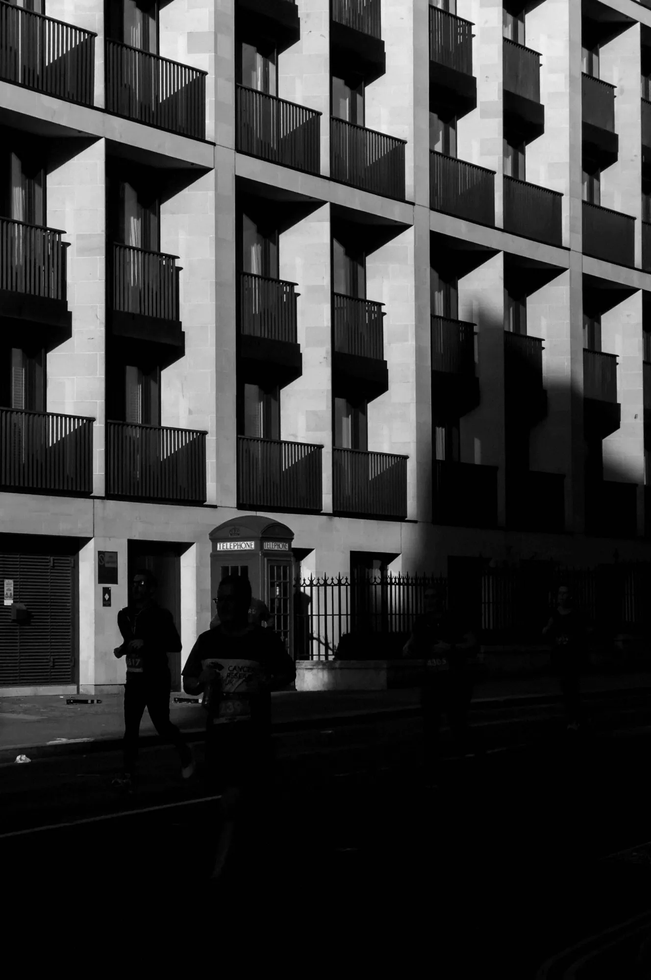 London Marathon runners in low sunlight passing a London telephone box beneath a block of flats.