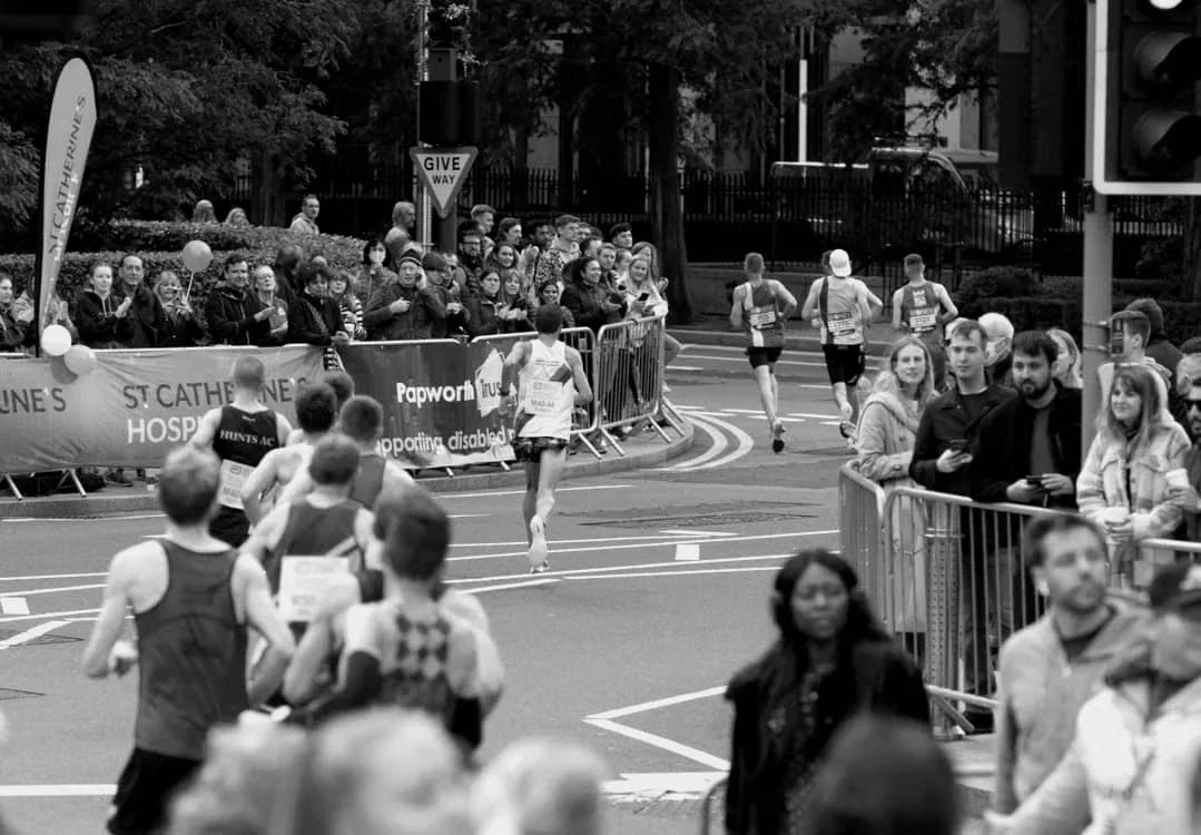 Spectators behind barriers cheering London Marathon runners at a road junction.