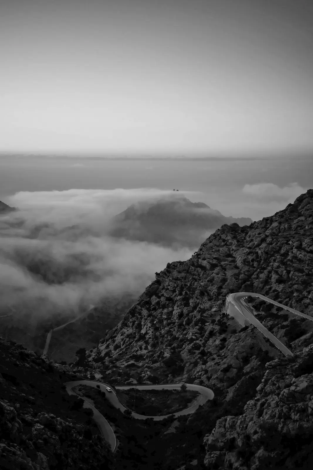 A road coiling down through the limestone of the Serra de Tramuntana, Mallorca, above low cloud.