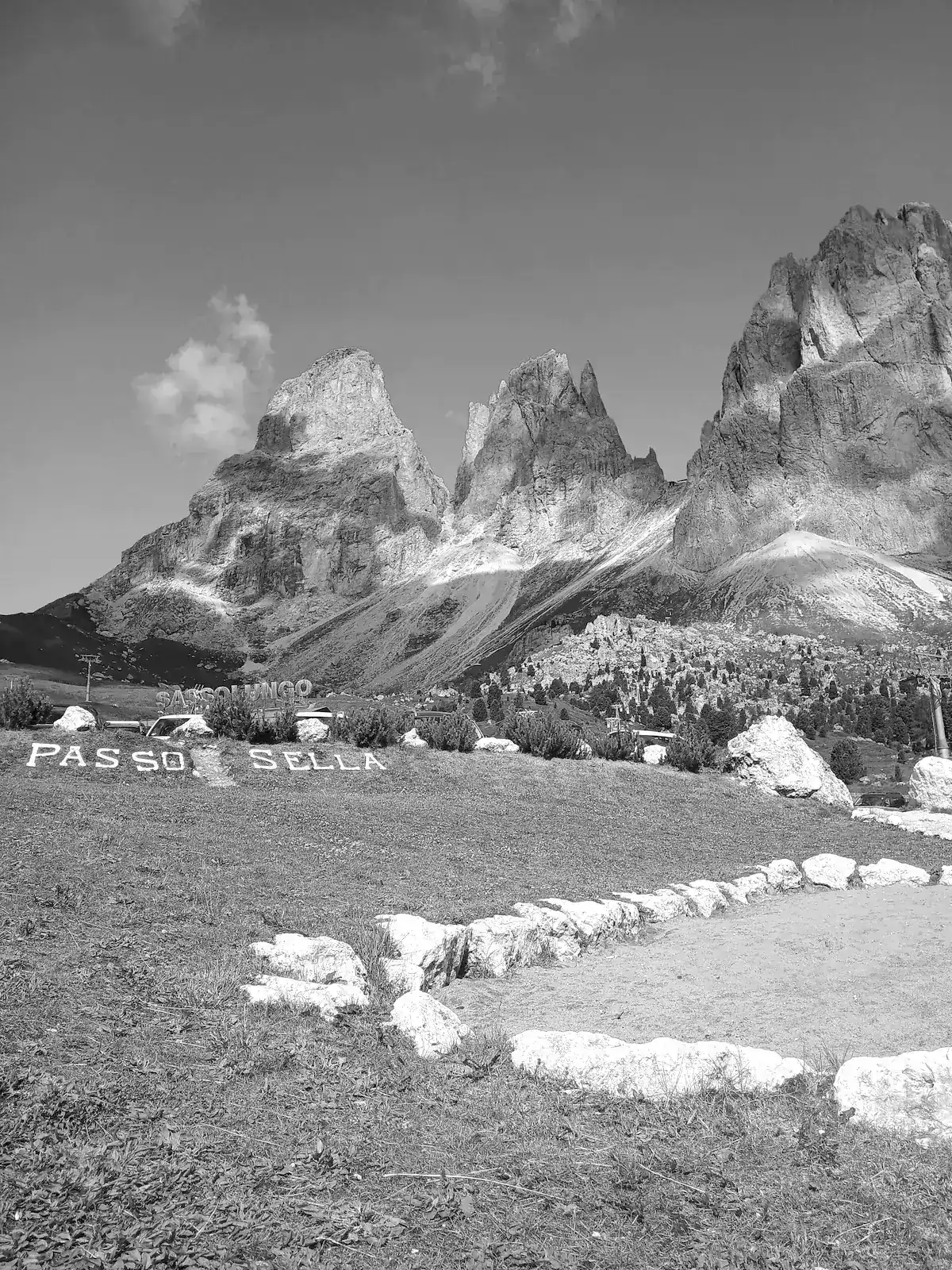 The towers of the Sassolungo group above the meadows at Passo Sella, with a sign for the pass in the foreground.