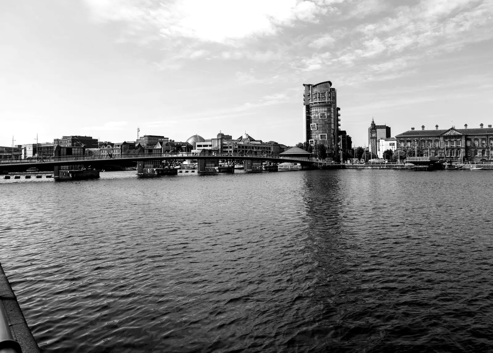 The River Lagan in Belfast, with the riverside skyline and a bridge on a bright day.