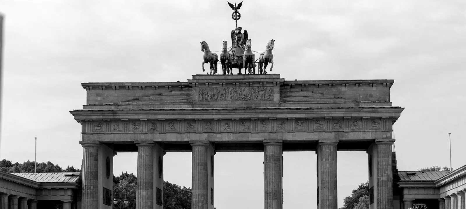 The Brandenburg Gate in Berlin with its four-horse statue against a cloudy sky.