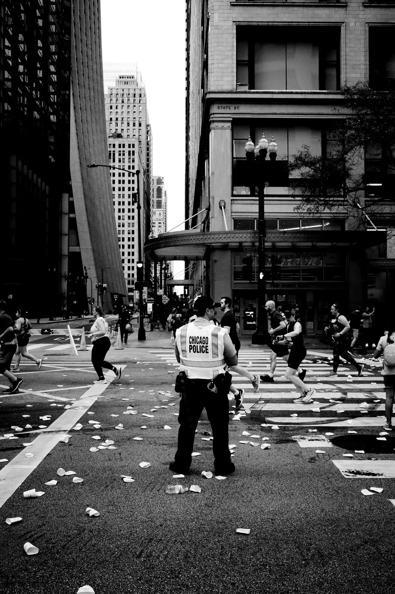 Chicago Marathon runners crossing a downtown street past a police officer, with paper cups on the road.