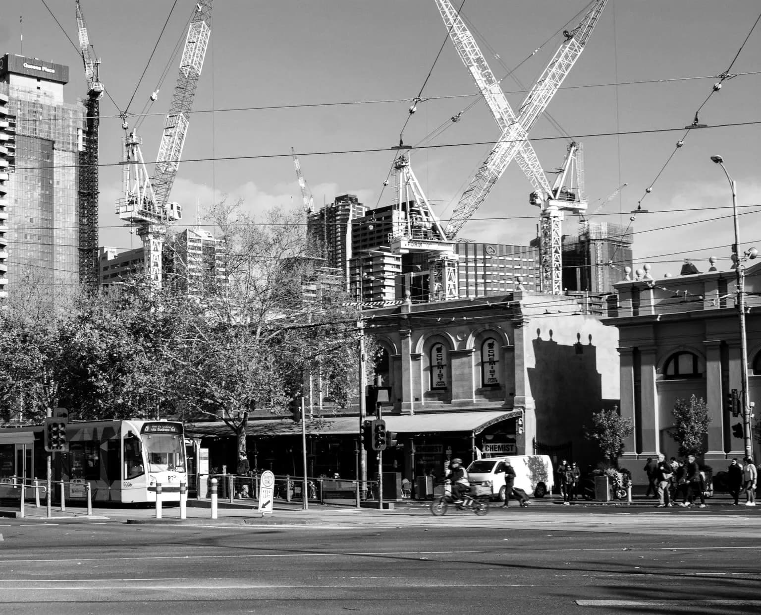 A tram on a Melbourne city street, with construction cranes and towers behind.